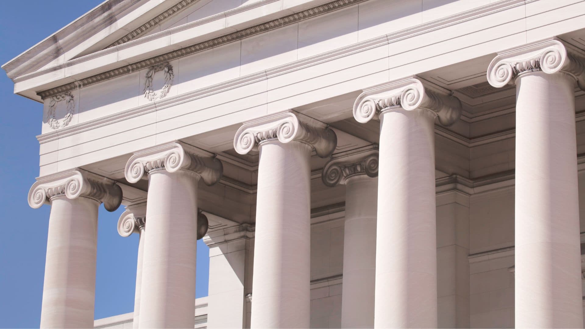 Classical white marble columns with Ionic capitals against blue sky, architectural detail photograph.