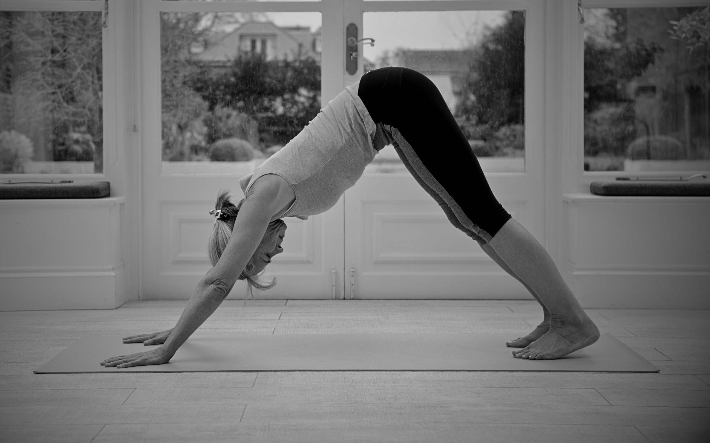Black and white photo of a person in a downward dog yoga pose on a mat, with focus on their hands and legs.