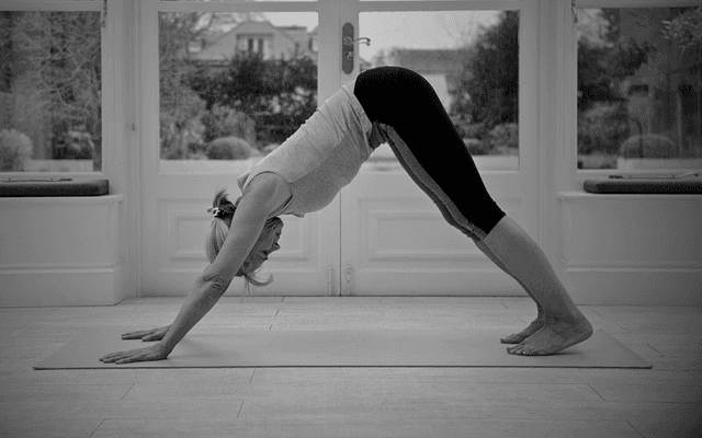 Black and white photo of a person in a downward dog yoga pose on a mat, with focus on their hands and legs.