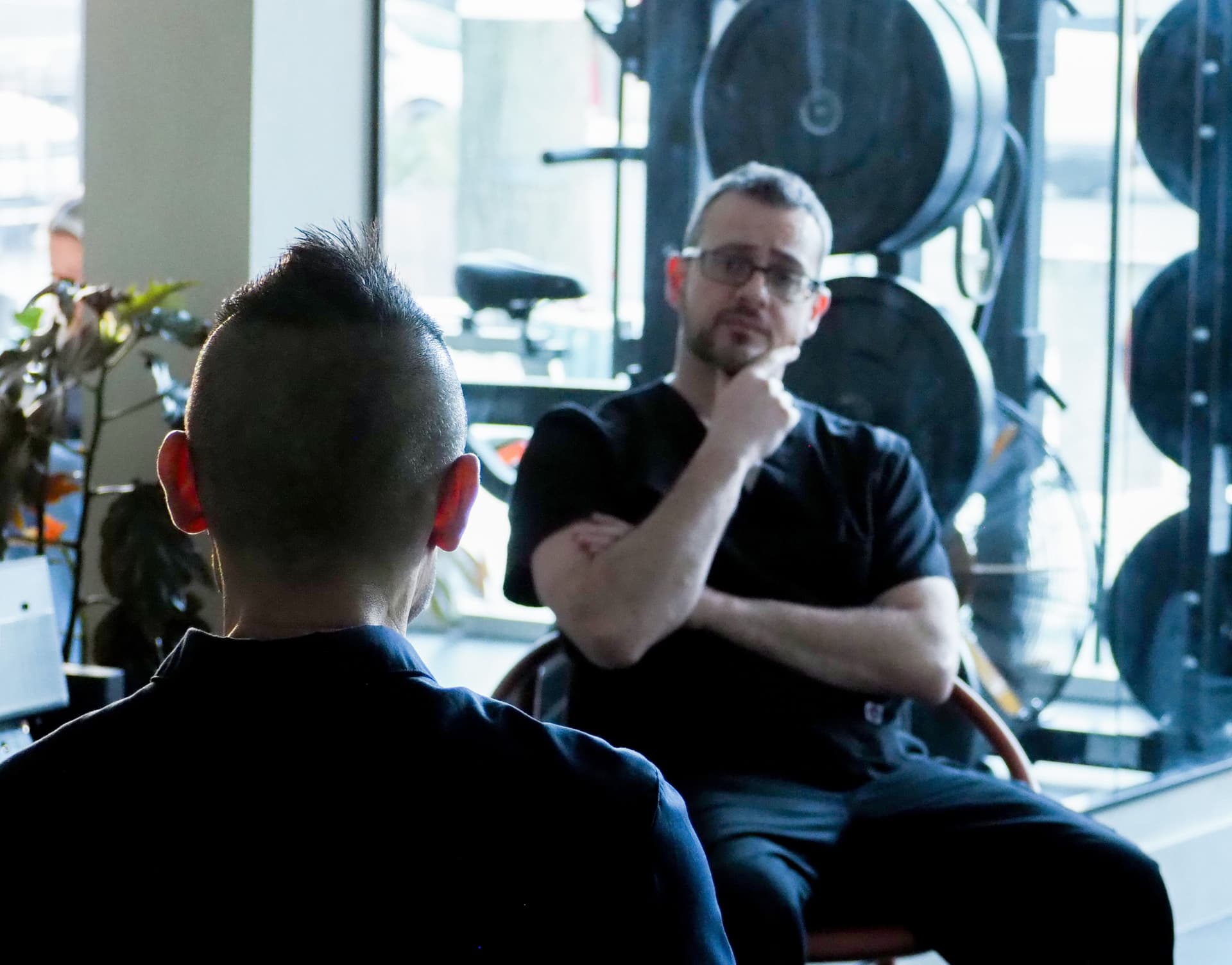 Photograph of two people having a meeting, one man is faced away from the camera, and the other is looking at him.