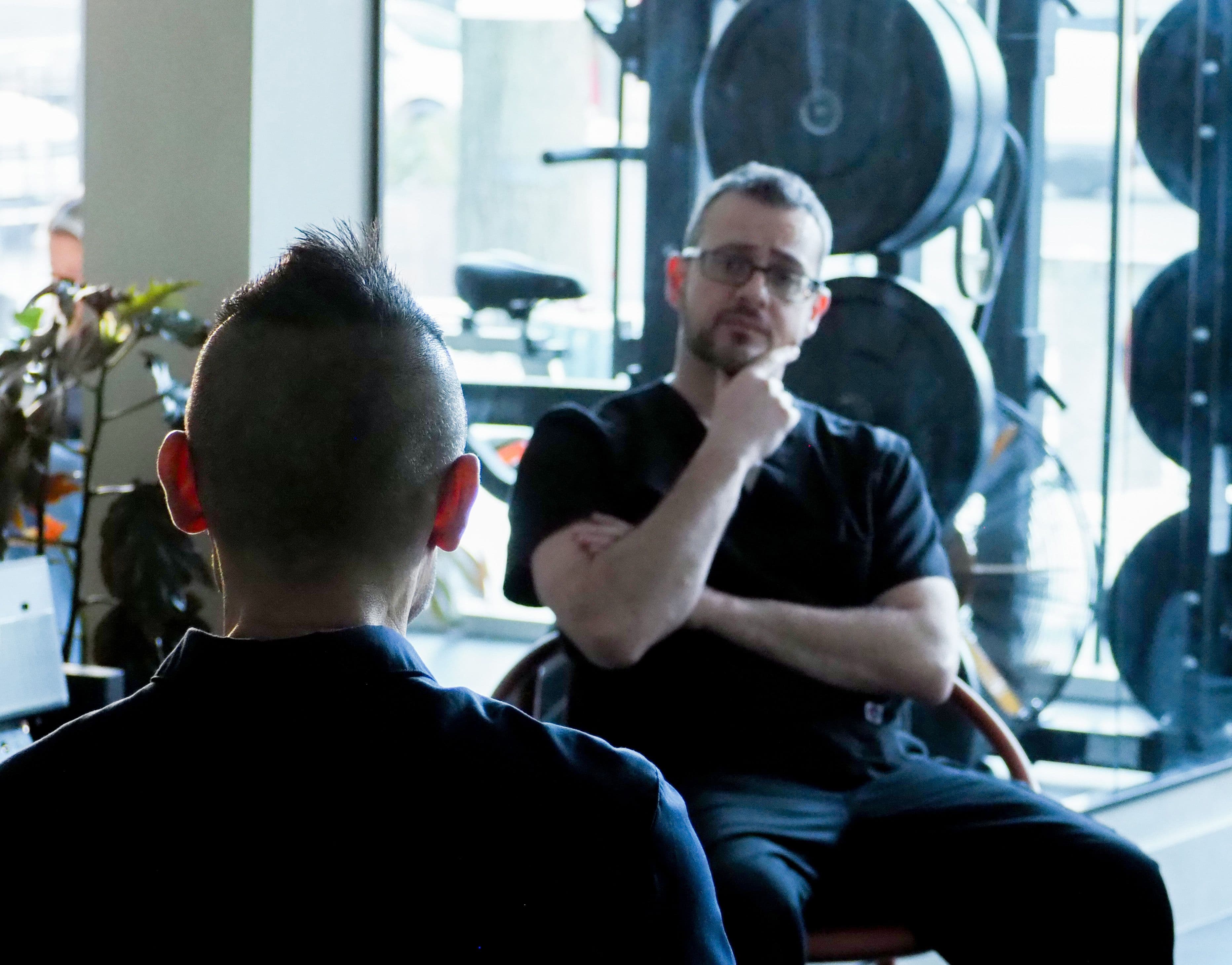 Photograph of two people having a meeting, one man is faced away from the camera, and the other is looking at him.
