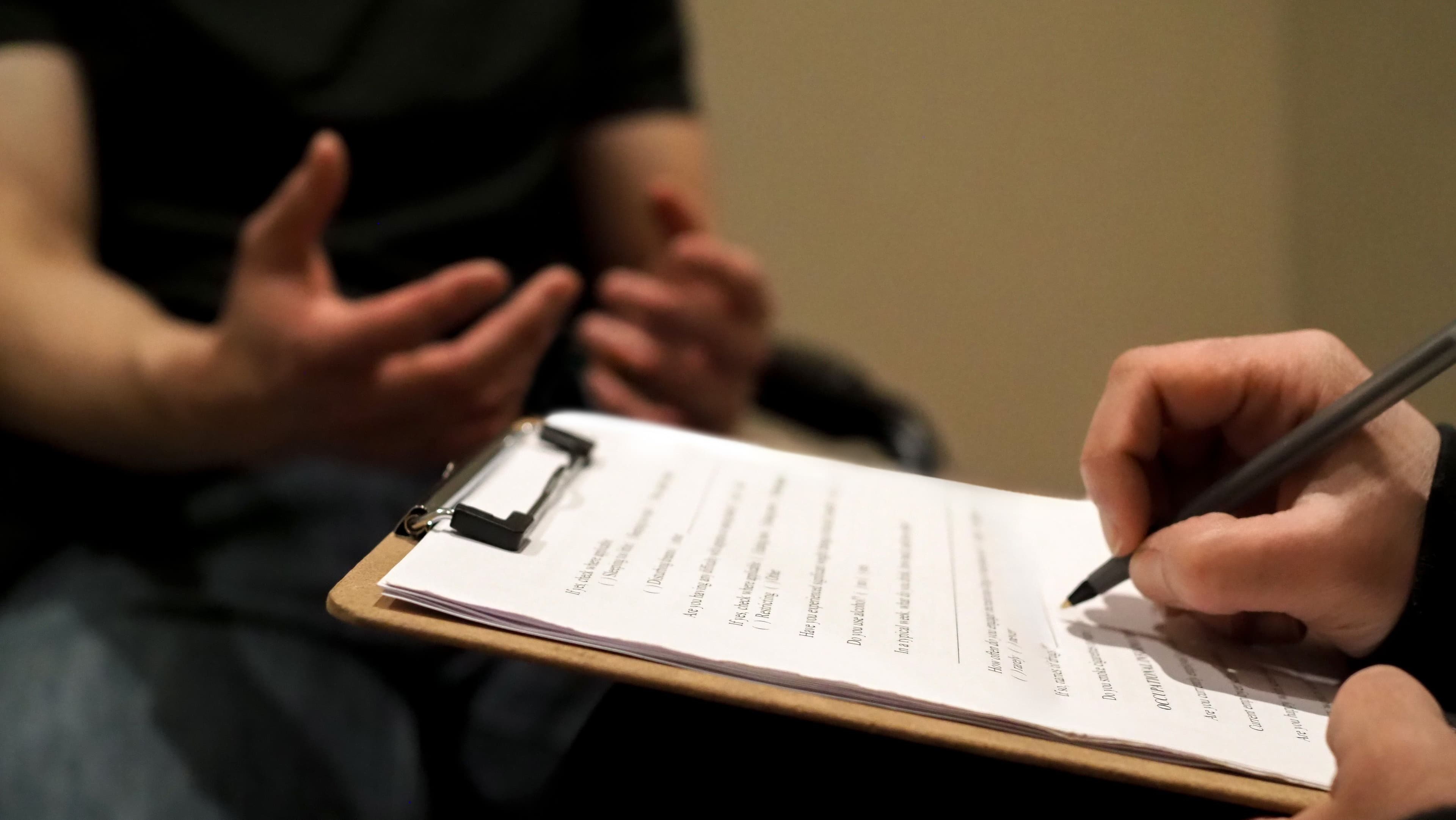 Photo of a therapist taking notes on a clipboard while listening to a client during a counselling session.