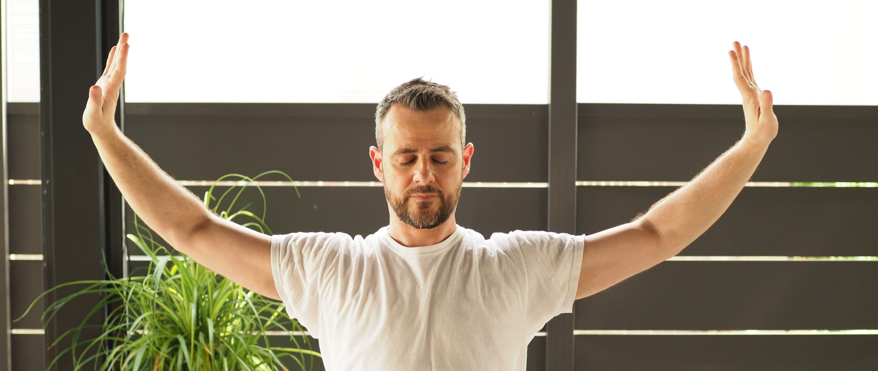 Dr. David Gabriele standing with both arms raised in a Tai Chi movement, in the Recovery Sanctuary at Curate Health.