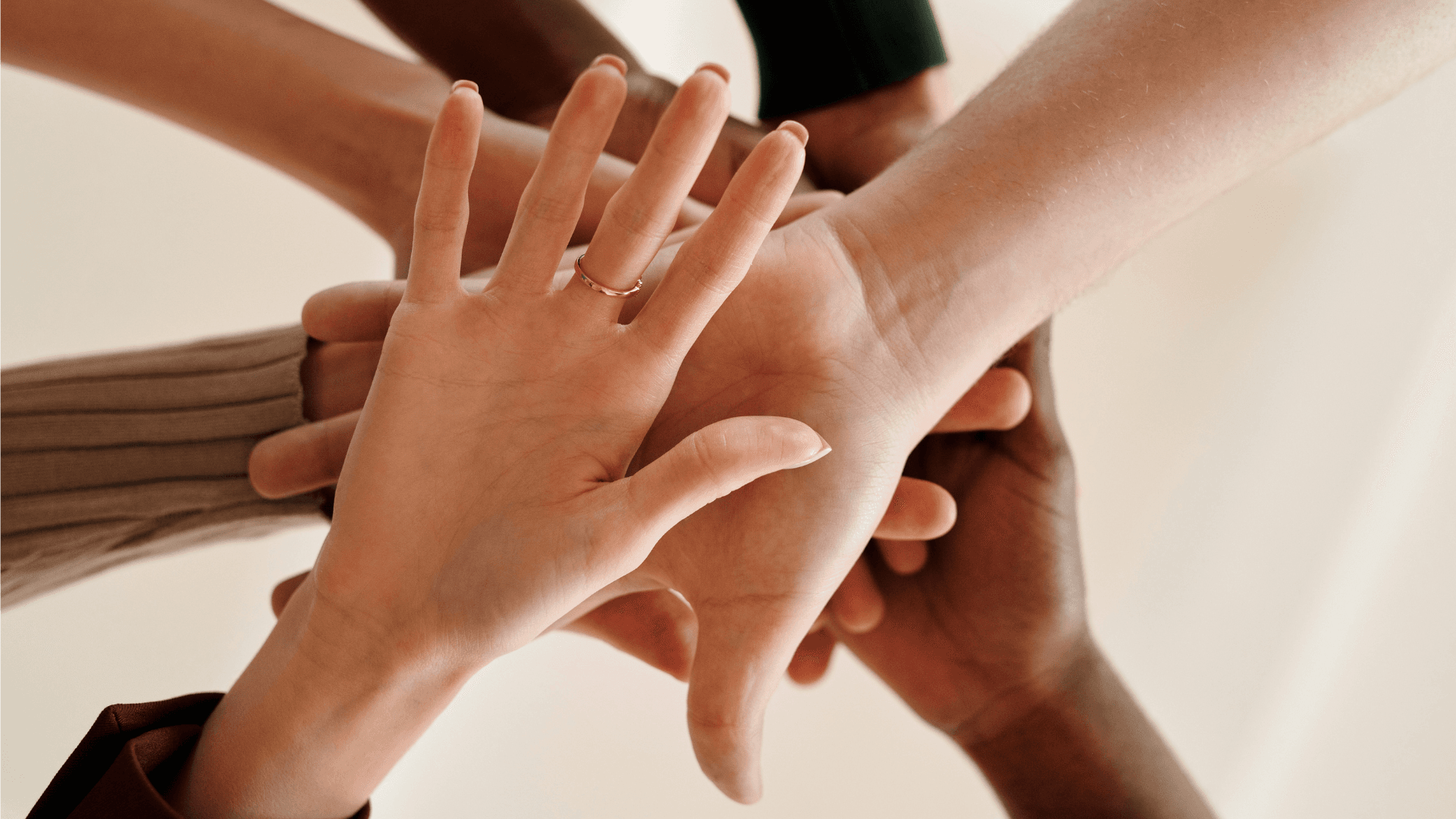 Diverse hands joining together in unity, close-up photograph against light background.