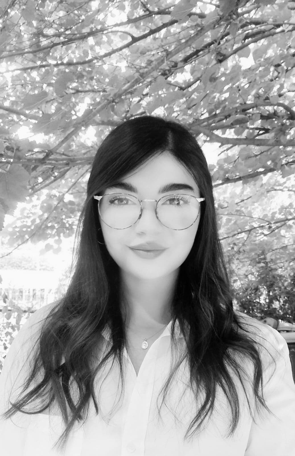 Black and white portrait of Safa Karoumi outdoors beneath a leafy tree.