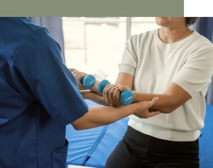 Photograph of healthcare professional assists a person using light dumbbells during rehabilitation.