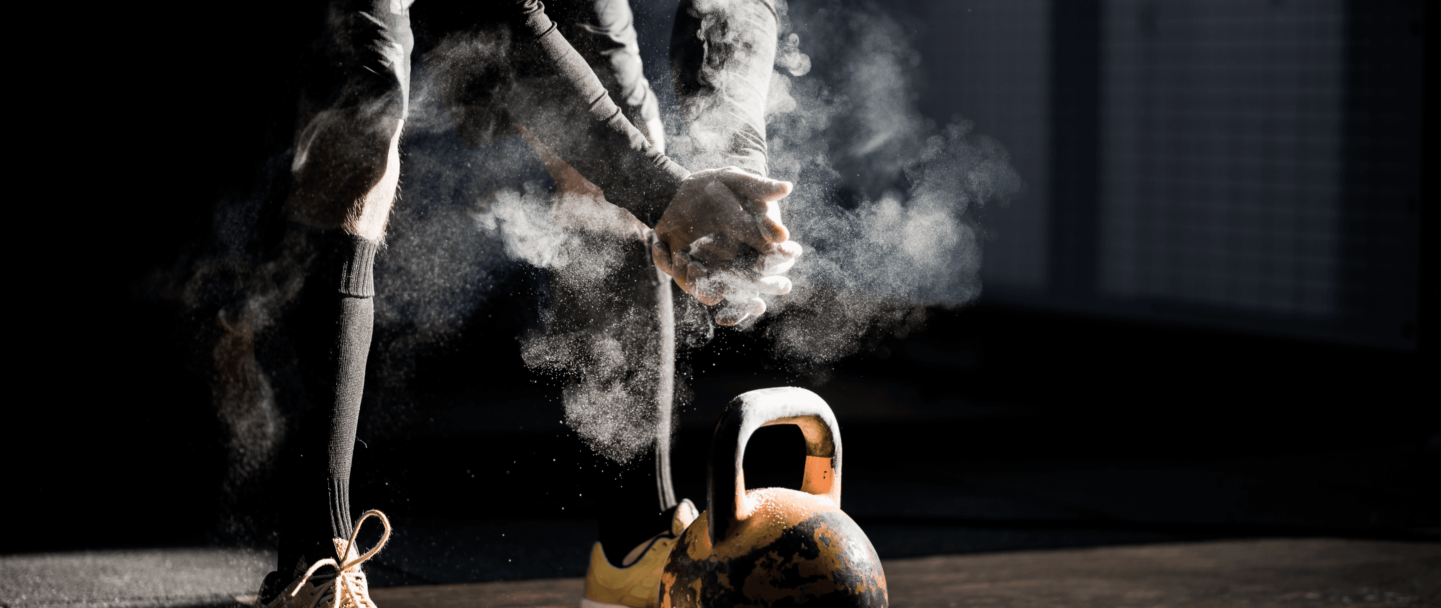Photo of a person preparing for a kettlebell workout, with chalk dust in the air, in a dimly lit gym setting.