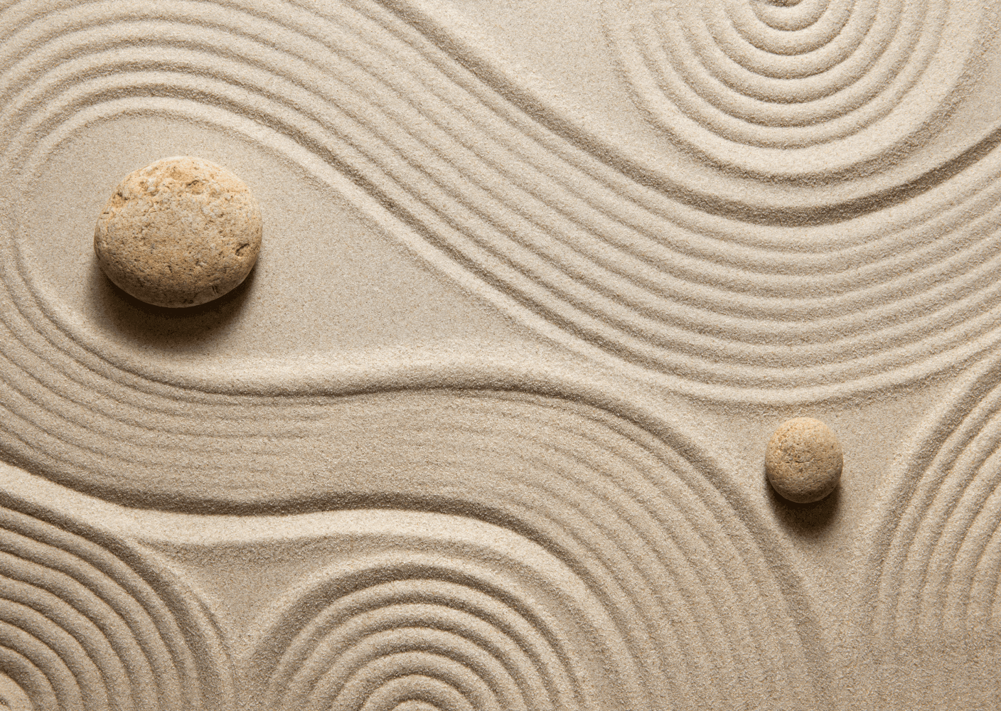A photo of a zen garden with two stones on sand featuring smooth, raked patterns.
