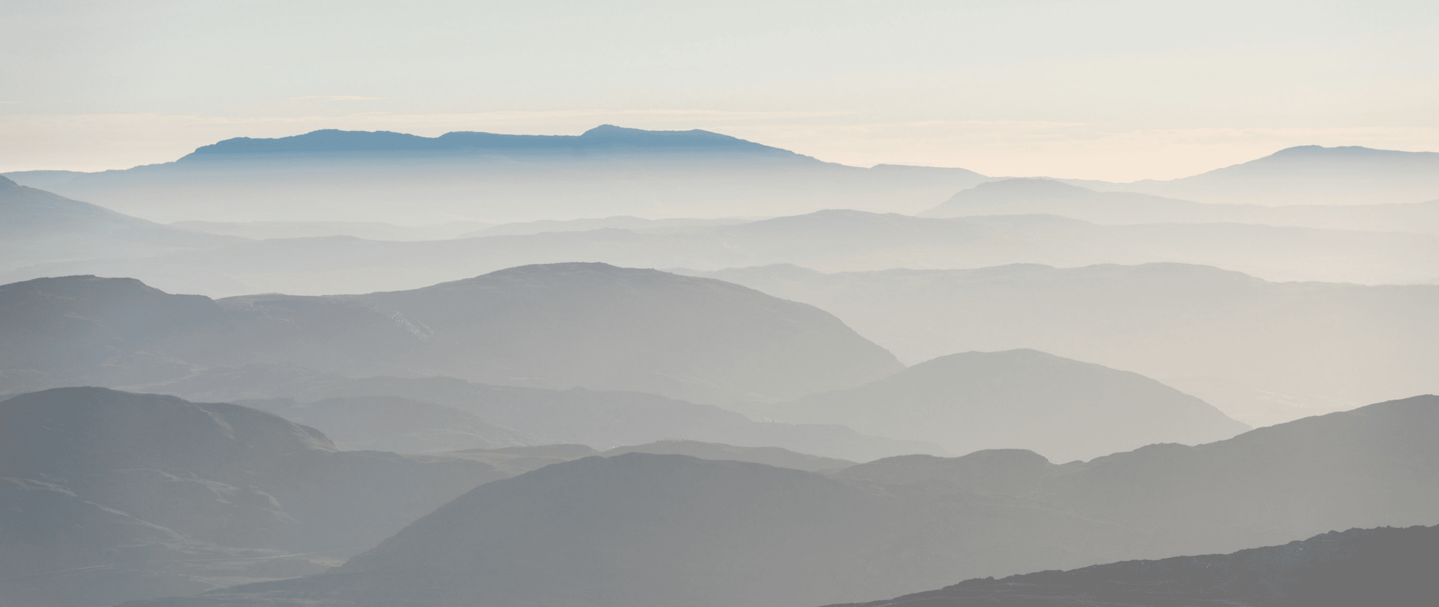 A serene photo of misty mountain layers under a soft sky, evoking a calm and tranquil atmosphere.