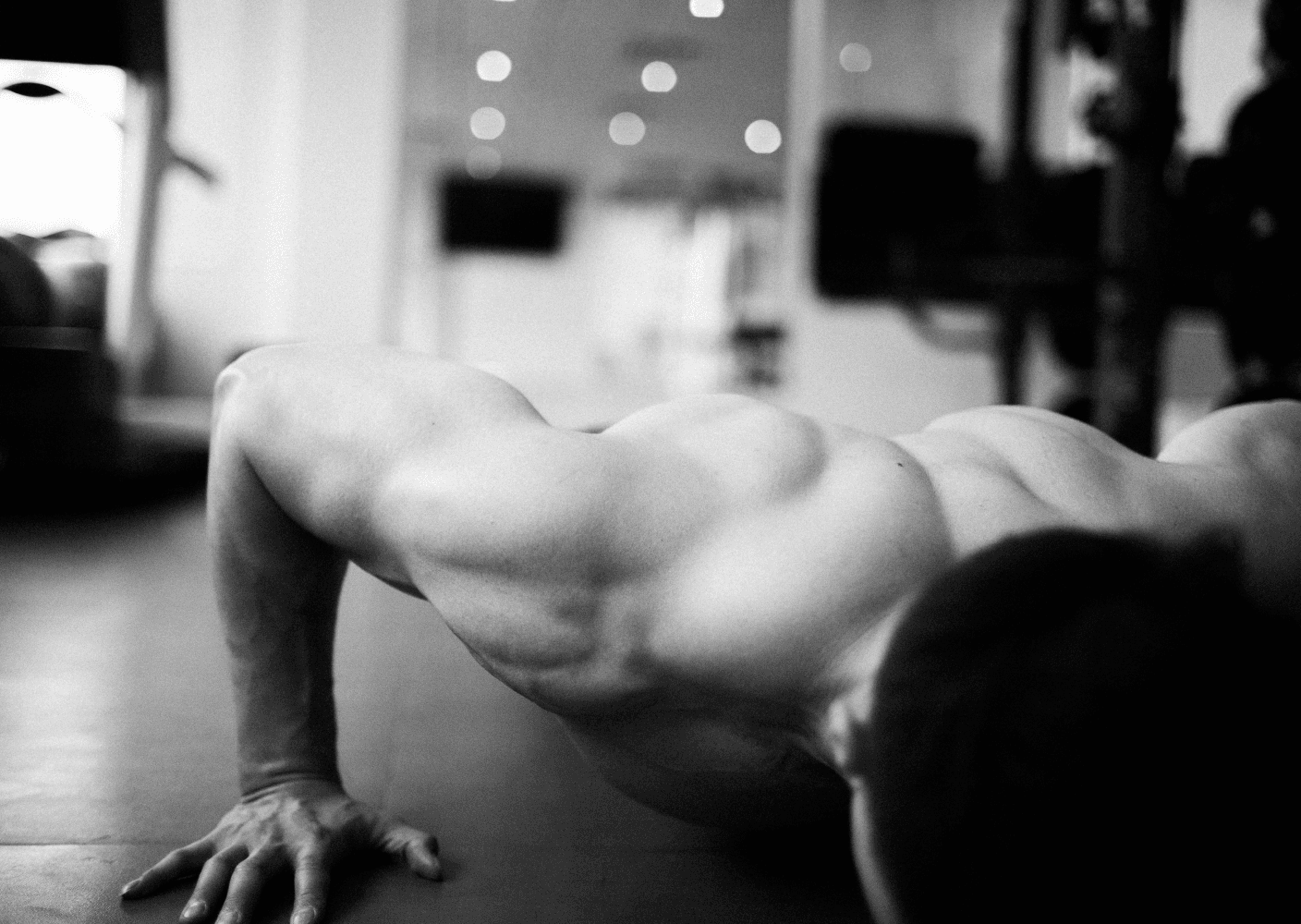 Black-and-white photo of a muscular man performing a push-up in a gym setting, focusing on arm and shoulder definition.