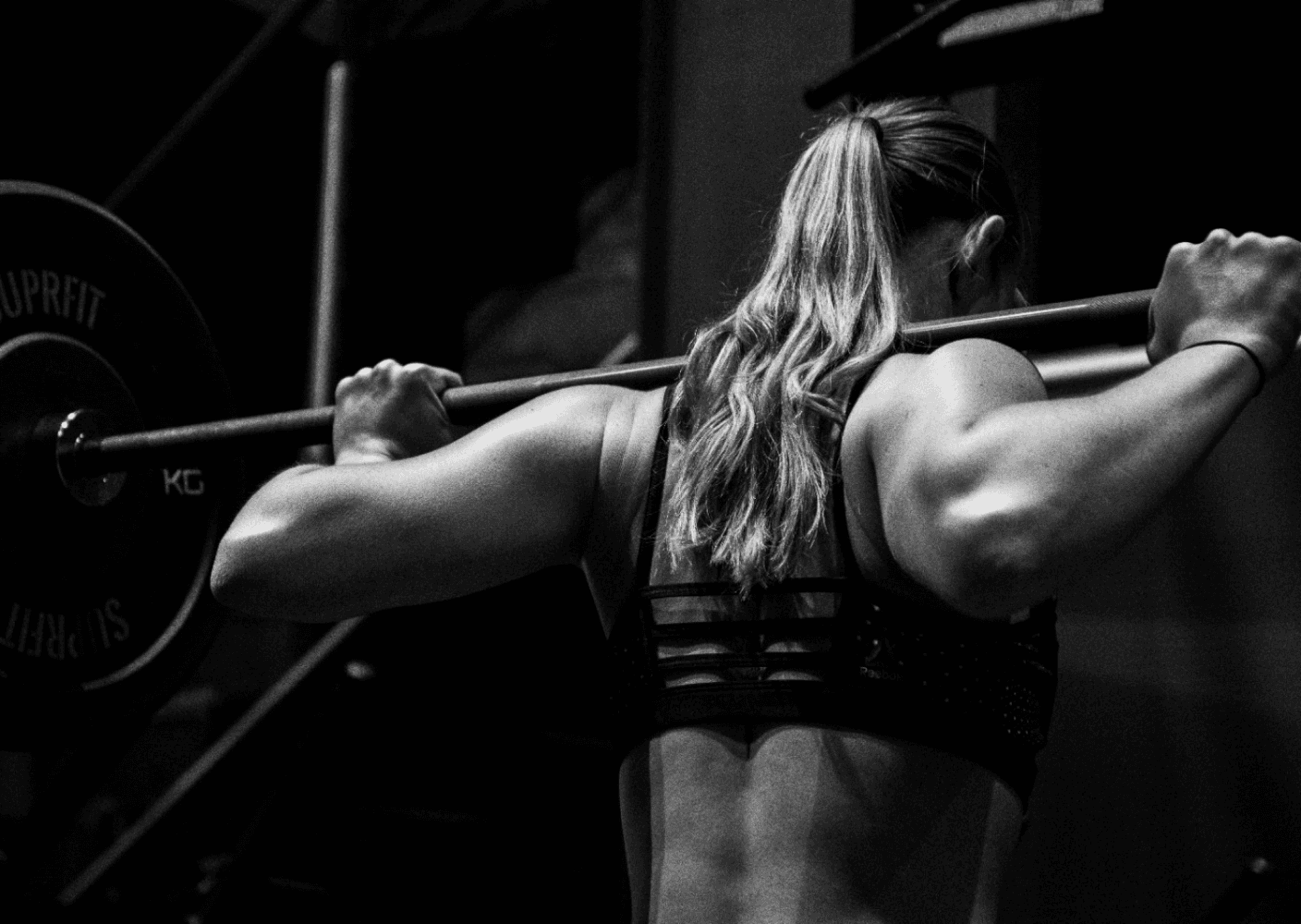 Black and white photo of a woman performing a barbell squat in a gym, showcasing strength and focus.