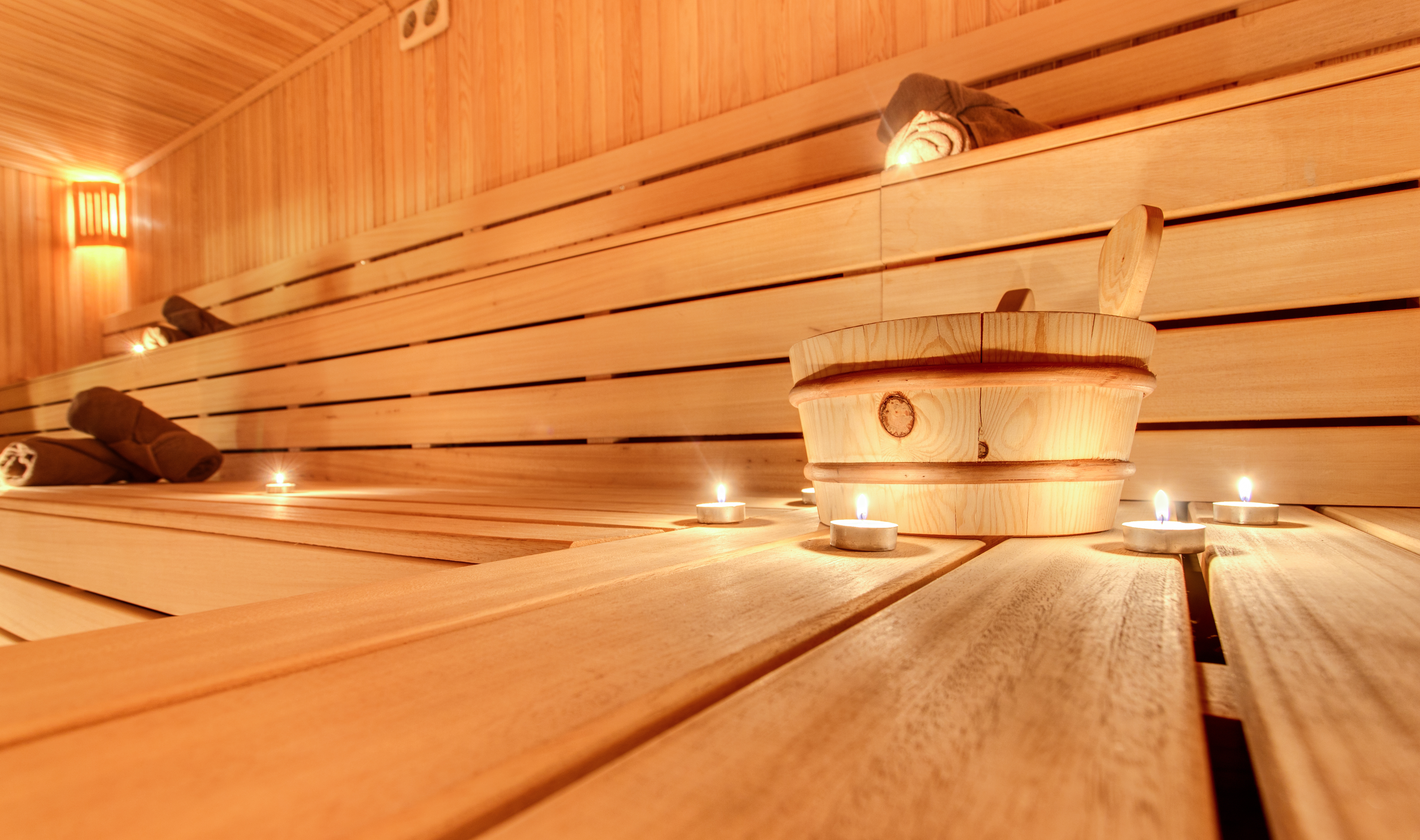 Photo of a sauna interior featuring wooden benches, a water ladle, and folded white towels for relaxation and heat therapy.