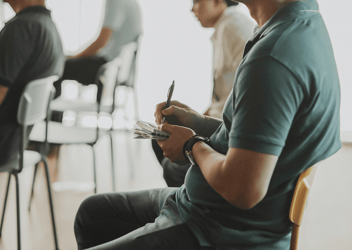 A participant taking notes during a group session, seated in a circle of chairs.