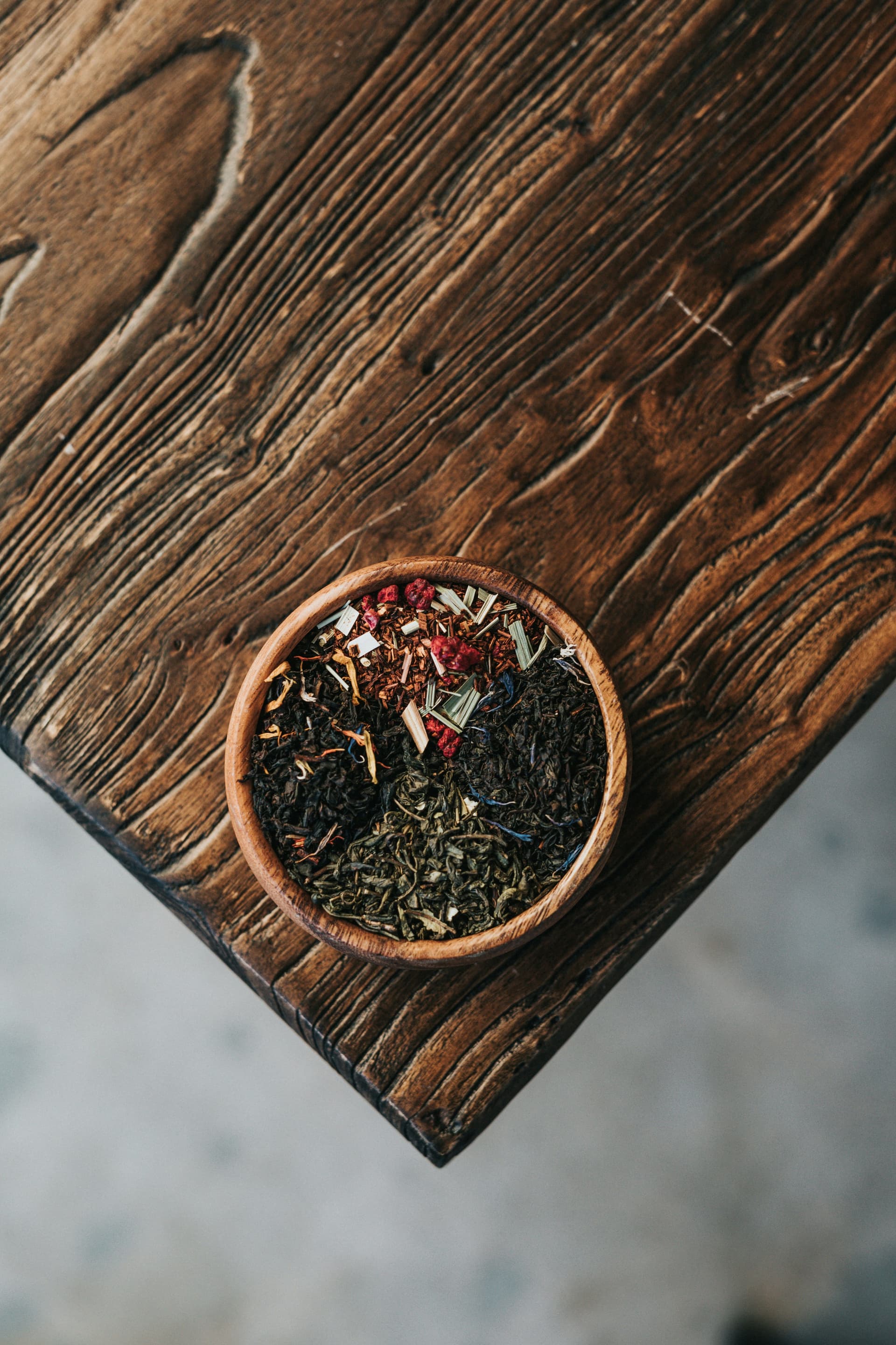 Photo of a bowl of dried herbs and spices on a wooden table, used in traditional Chinese medicine.